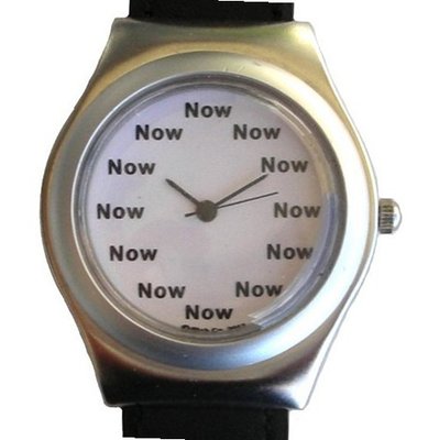 "Now" Is the Time That Is Shown Each Hour on the White Dial of the Brushed Chrome Round Tonneau Shape with a Black Leather Strap